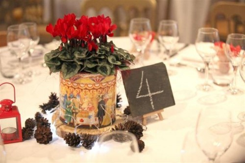 a bold winter wedding centerpiece of red blooms in a large box on a wood slice and pinecones around is a simple and cute idea