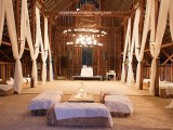 a very rustic barn wedding reception with hay stacks, wooden tables and white curtains plus oversized chandeliers with candles