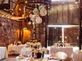 a chic barn wedding reception space with a chandelier with yarn balls, bold blooms, lights and neutral linens is all chic