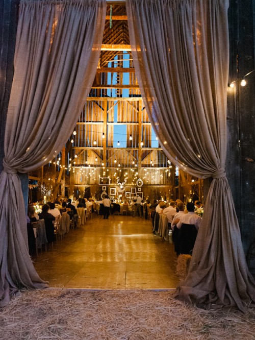 a cozy barn wedding reception space with lights and grey curtains is elegant and stylish