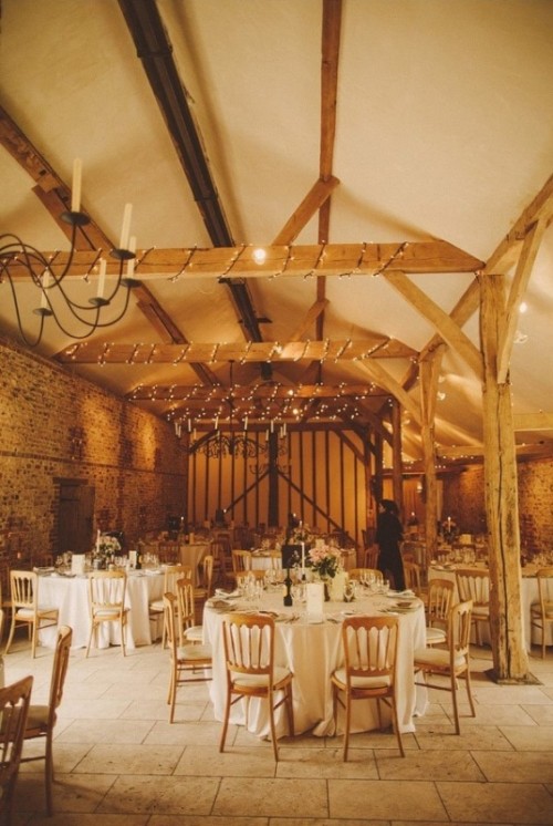 a barn wedding reception space with lights, chandeliers, neutral linens and blooms