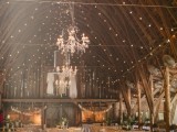 a barn wedding reception with multiple lights and chandeliers, greenery and banners all around the space