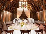 a barn wedding reception space with neutral linens, bright blooms and greenery and curtains for a backdrop