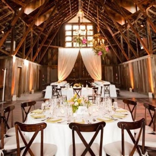 a barn wedding reception space with neutral linens, bright blooms and greenery and curtains for a backdrop