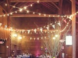 a barn wedding reception with lights, white bannets, branches with candles, bright flowers, colorful garlands