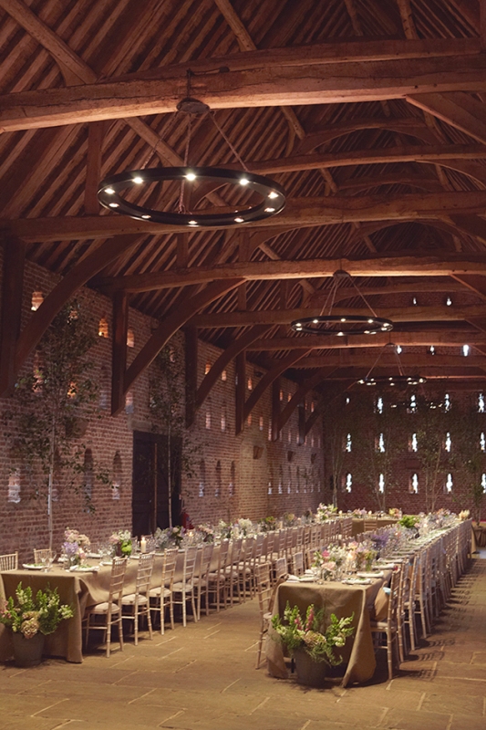 a simple wedding reception space with chandeliers, greenery, trees, neutral blooms and neutral linens