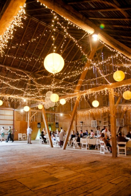 a simple barn wedding reception decorated with lots of lights, paper lamps and yarn ones is a very cozy space