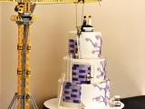 a white Lego wedding cake with purple bricks, purple blooms, cake toppers and a stationary hoist