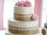 a white textural buttercream with burlap and white lace plus pink blooms and a bunting topper is a stylish rustic idea