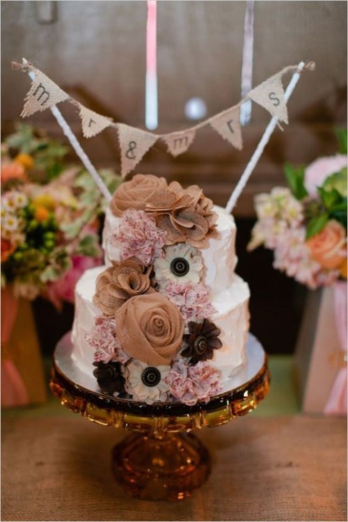 a white textural wedding cake with fabric blooms and a burlap bunting is a cool rustic dessert