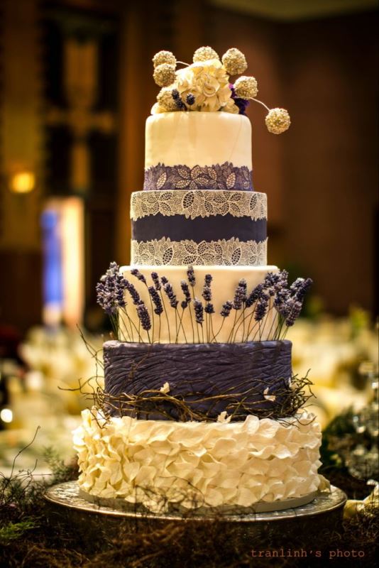 A refined rustic wedding cake in white and purple, with lace, sleek and textural tiers and some lavender and vine