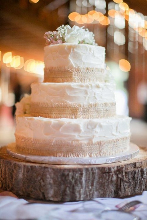 a simple and cool white textural buttercream wedding cake with burlap and white blooms on top is rustic classics