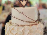 a white wedding cake with a leaf and a sleek tier and a heart wood burnt topper for a rustic feel