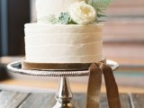 a neutral buttercream wedding cake with a white bloom and greenery and beige velvet ribbon for a delicate and refined accent