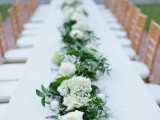 a greenery and white bloom table garland and some candles that match it