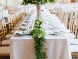 a greenery garland with some neutral blooms and a lush and tall greenery centerpiece enliven the table