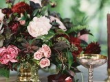 an exquisite summer wedding tablescape with a lush floral centerpiece with blush and marsala blooms, a marsala and a gold glass and chic linens in pink