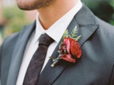 a red and marsala wedding boutonniere with greenery is a bright and chic accent for a fall groom’s look