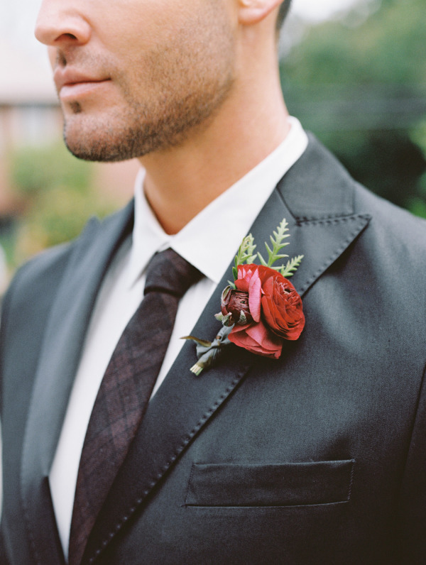 A red and marsala wedding boutonniere with greenery is a bright and chic accent for a fall groom's look