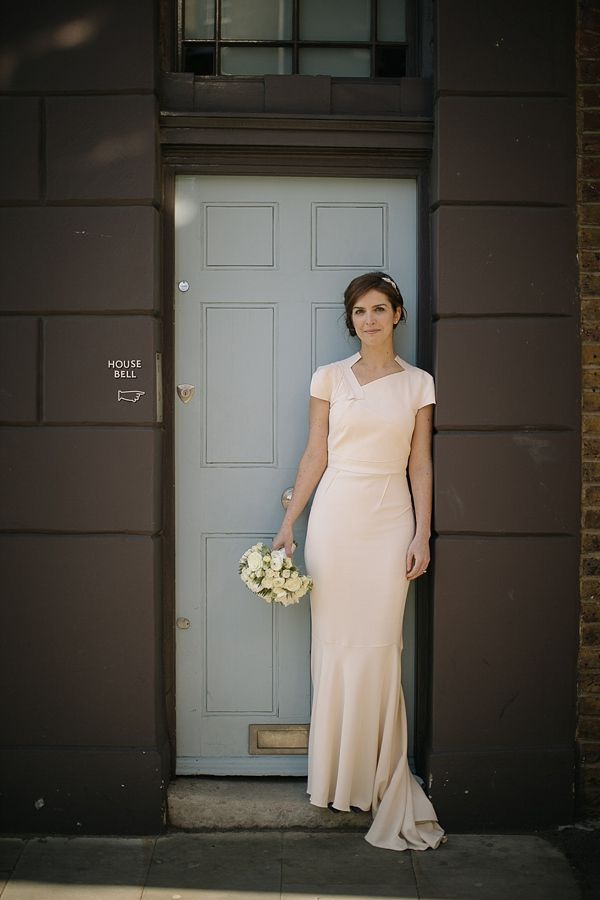A blush minimalist sheath wedding dress with a geometric neckline, short sleeves and a train is romantic