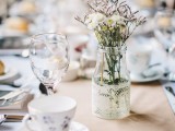 a clear vase wrapped with white lace, with dried herbs and flowers plus a table name
