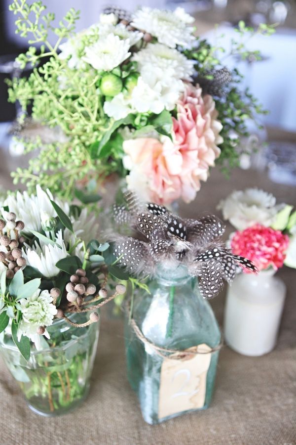 Bright and neutral blooms, greenery, feathers all palced into clear glass vases is a lush and chic barn centerpiece