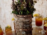 a bark wrapped vase with greenery and dark foliage is a cozy rustic wedding centerpiece