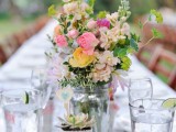 a neutral barn wedding centerpiece of pastel and yellow blooms, greenery and a succulent in a pot