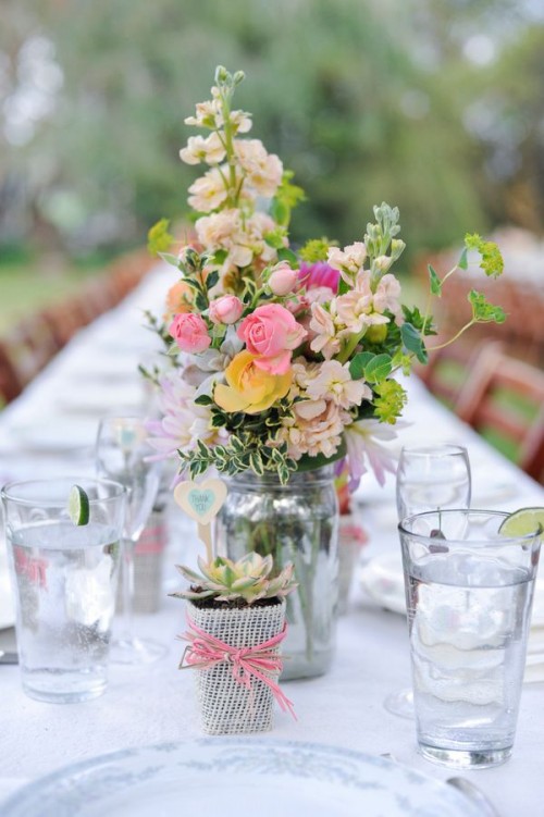 a neutral barn wedding centerpiece of pastel and yellow blooms, greenery and a succulent in a pot