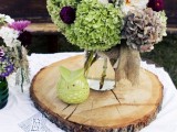 a wood slice with a green owl candleholder and a jar with bright and bold blooms