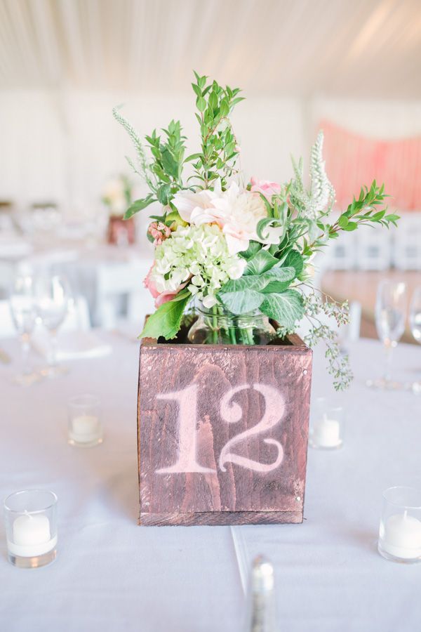 A plywood box with a table number and pastel blooms and greenery is a cool barn wedding centerpiece idea
