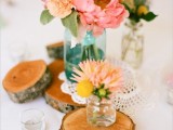 a bright wedding centerpiece of wood slices, a doily and pastel blooms in jars