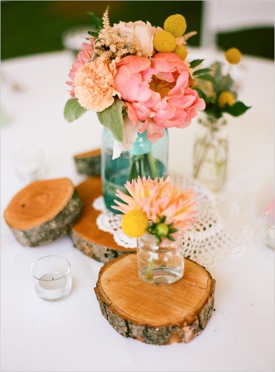 A bright wedding centerpiece of wood slices, a doily and pastel blooms in jars