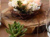 a wood slice with a succulent, a nest with white blooms and white candles is a nice centerpiece for a barn wedding