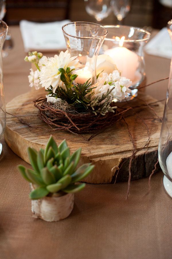 A wood slice with a succulent, a nest with white blooms and white candles is a nice centerpiece for a barn wedding