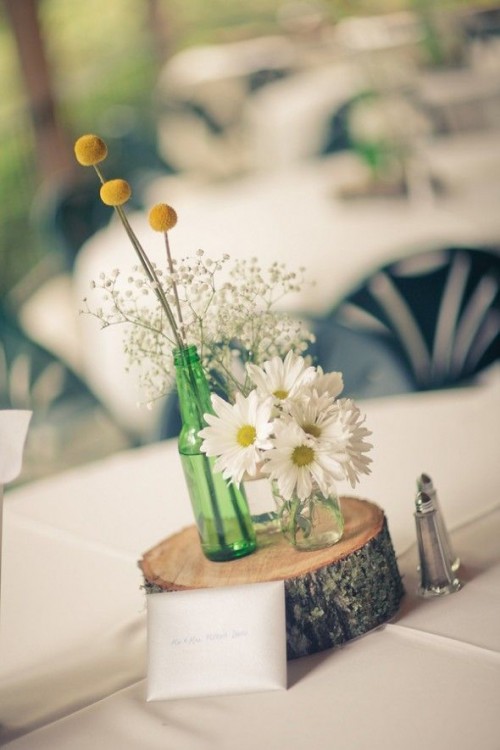 a wood slice with white blooms and billy balls plus a table name is a stylish idea for a wedding centerpiece