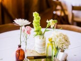 a barn wedding centerpiece with bottles and jars, white, pink and green blooms, a stack of books and some fabric