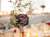 a barn wedding centerpeice of a jar with greenery, blooms and cabbages plus candles around looks very rustic