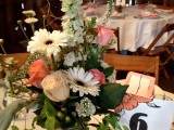 a lush floral wedding centerpiece of white and pink blooms, greenery and foliage and a table number