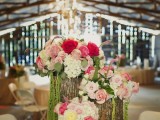 tree stumps with white and pink blooms plus cascading greenery make up a cool barn wedding centerpiece