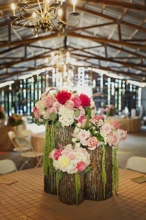 tree stumps with white and pink blooms plus cascading greenery make up a cool barn wedding centerpiece