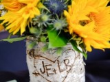 a vase wrapped with cutout bark and yellow blooms and thistles for a bright and cheerful wedding centerpiece