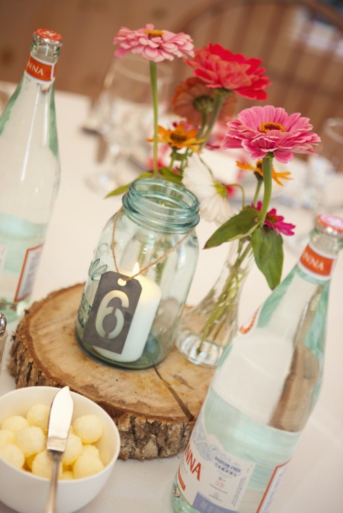 a candle in a har with a tag, a wood slice and some bright pink blooms for a barn wedding centerpiece