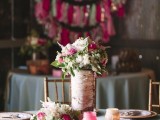 a rustic wedding centerpiece of white and pink blooms with greenery in a vase wrapped with bark