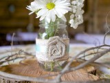 a wood slice with a jar with a fabric bloom and some white blooms in it for a cute barn wedding centerpiece