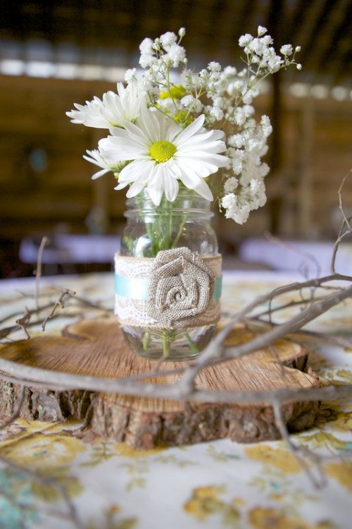 a wood slice with a jar with a fabric bloom and some white blooms in it for a cute barn wedding centerpiece