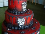 a red Day of the Dead wedding cake with black dripping, sugar skulls and a skull in a sombrero