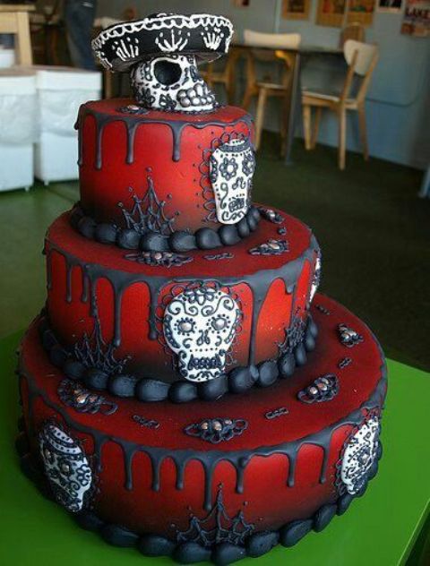 a red Day of the Dead wedding cake with black dripping, sugar skulls and a skull in a sombrero