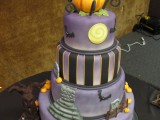 a creative purple wedding cake with a striped tier and graveyard and bat ones, with a scary tree and stacked pumpkins on top for a Halloween wedding