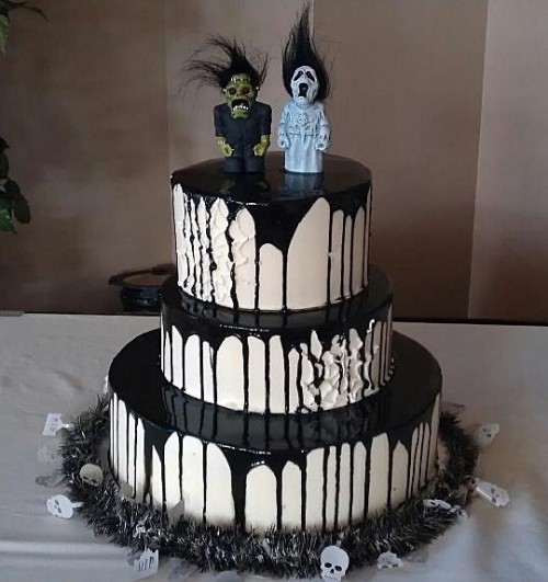 a round white wedding cake with black dripping and scary toppers on top looks spooky and very statement-like